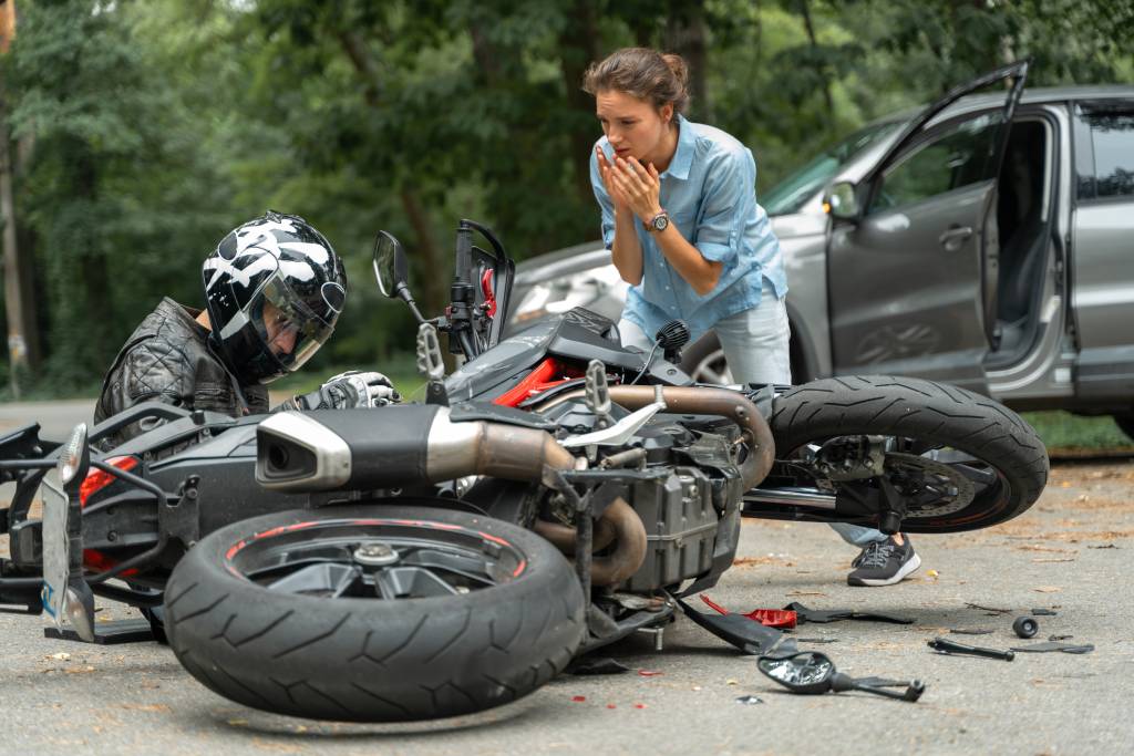 A motorcyclist on the ground while a driver looks on.